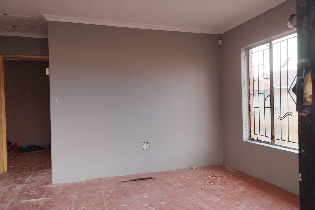 An empty living room featuring tiled flooring, coved ceilings, and a window with security bars, presenting a blank canvas for renovation.
