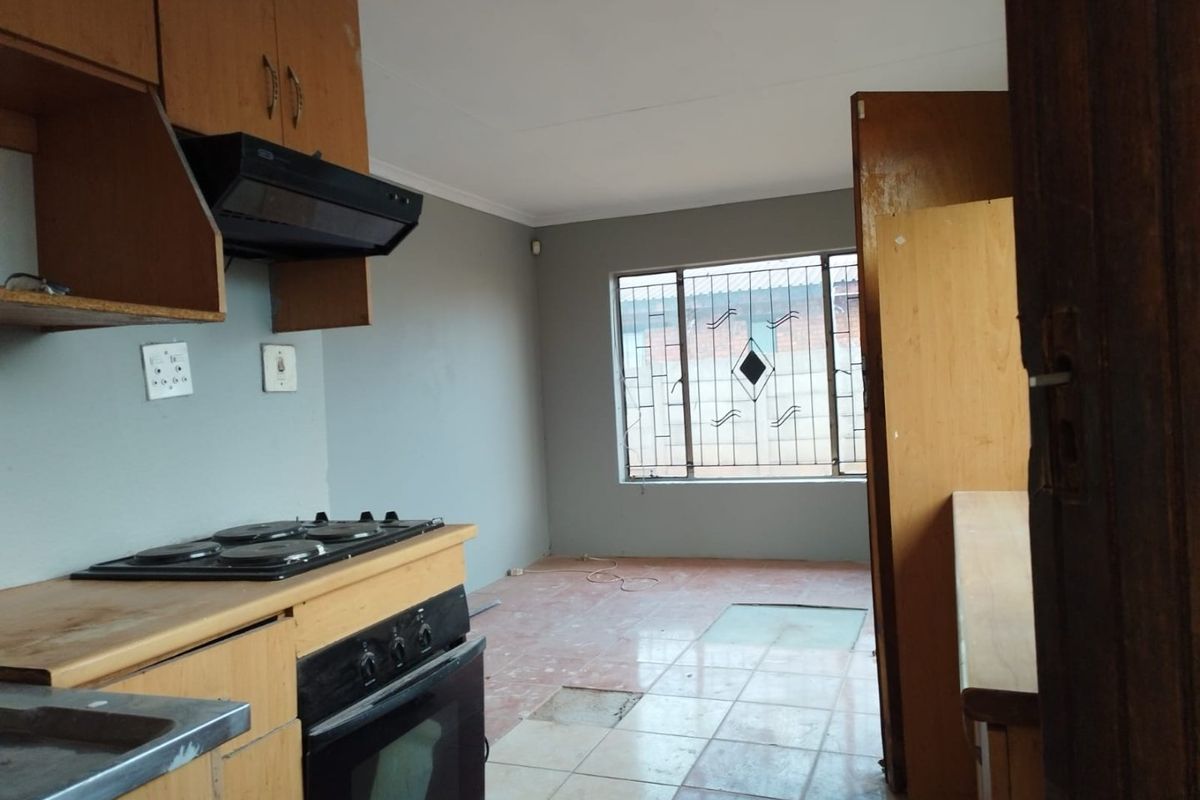 A functional kitchen space featuring built-in cabinetry, an integrated oven and hob, and security bars on the window. The flooring requires repair.