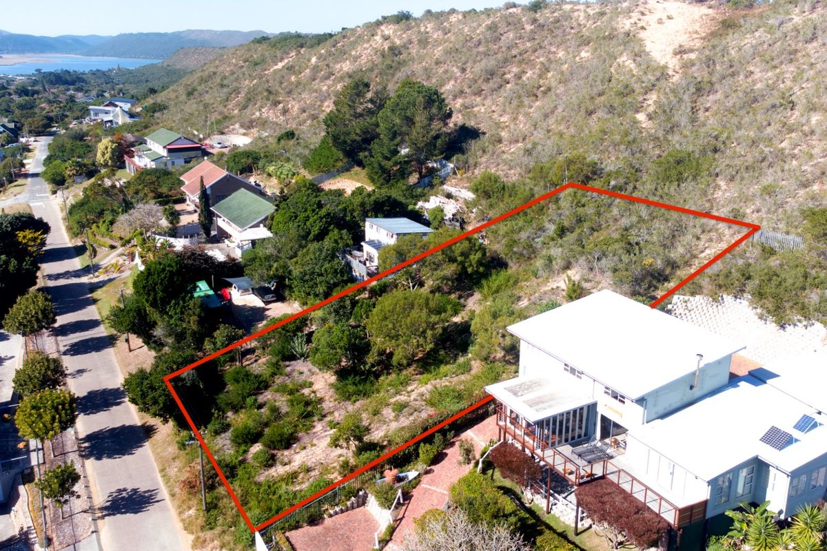 Aerial view of a vacant residential plot featuring sloped terrain and established vegetation, situated in a coastal neighborhood setting.