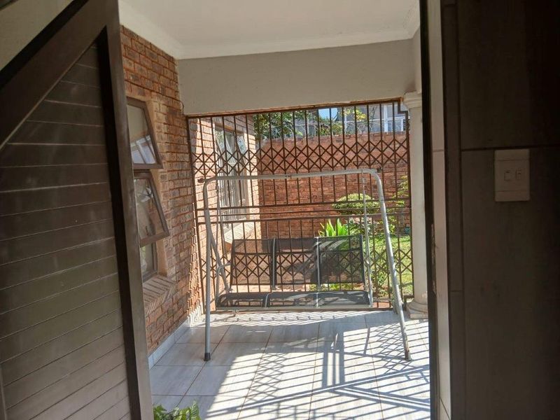 A covered patio area featuring exposed brick walls, tiled flooring, and secure metal security bars overlooking the garden.