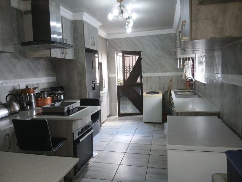 A functional kitchen featuring modern grey cabinetry, built-in oven and hob, extractor fan, tiled finishes, and direct access to an exterior area.