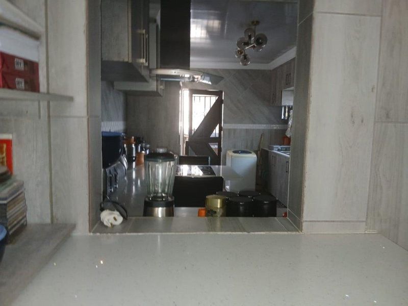 A view through a service window into a functional kitchen featuring tiled walls, built-in cabinetry, and stone countertops.