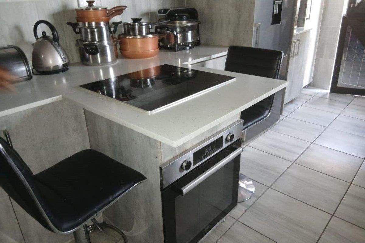 Modern kitchen featuring a built-in oven, electric hob, stone countertops, and subway tile backsplash with neutral tiled flooring.