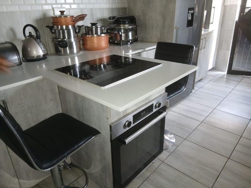 Modern kitchen featuring a built-in oven, electric hob, stone countertops, and subway tile backsplash with neutral tiled flooring.