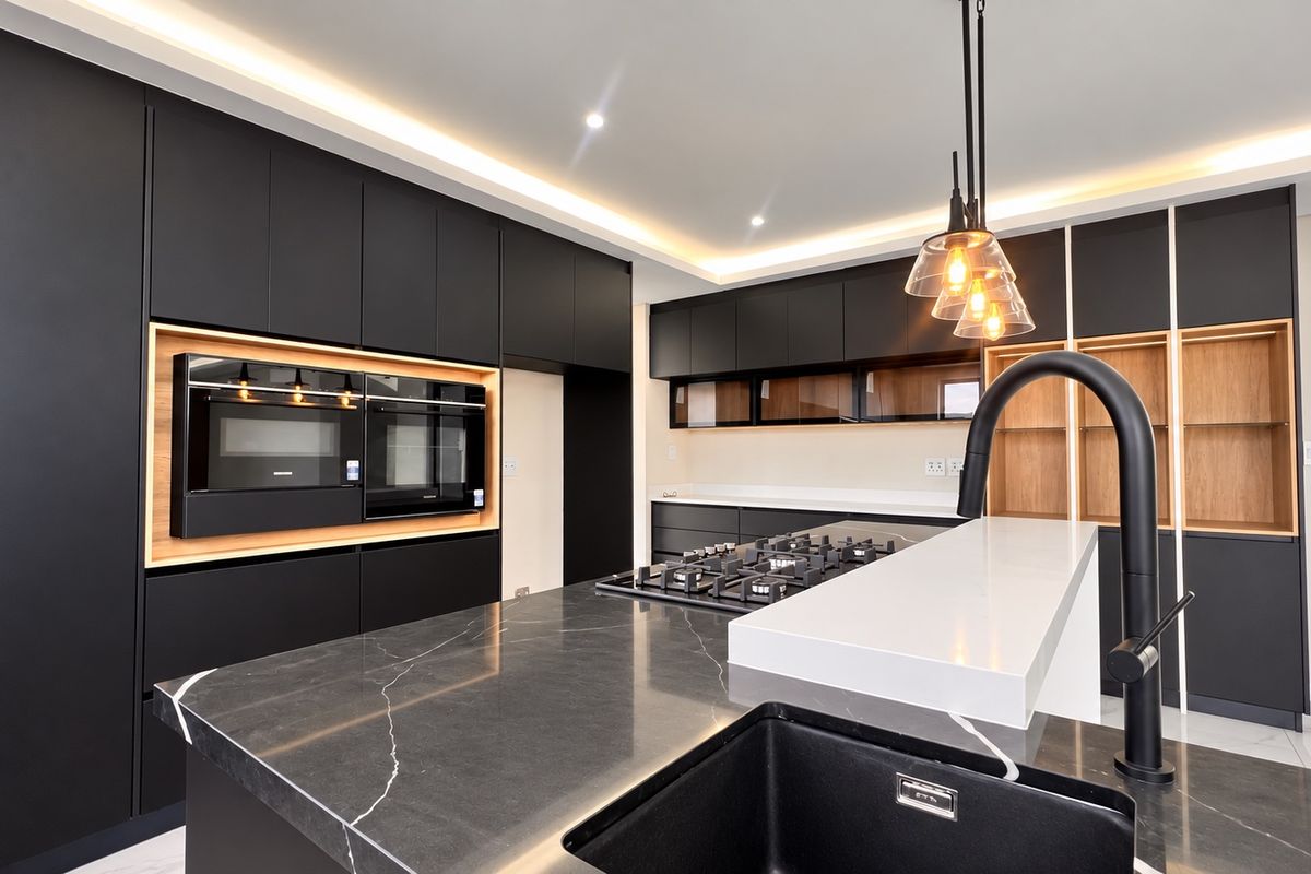Modern kitchen featuring matte black cabinetry, stone countertops, a central island with a gas hob, and integrated high-end appliances with ambient cove lighting.