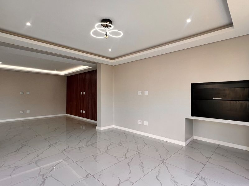 Spacious open-plan living area featuring modern porcelain tile flooring, recessed ceiling lighting, cove lighting, and a sleek built-in fireplace with wood slat feature wall.