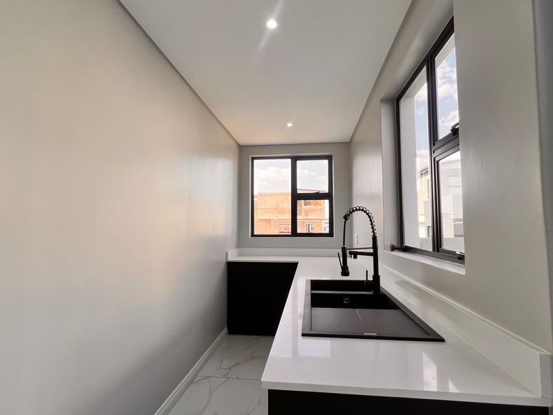 A modern, minimalist scullery featuring sleek black cabinetry, white quartz countertops, a double sink with a black faucet, and bright recessed lighting.