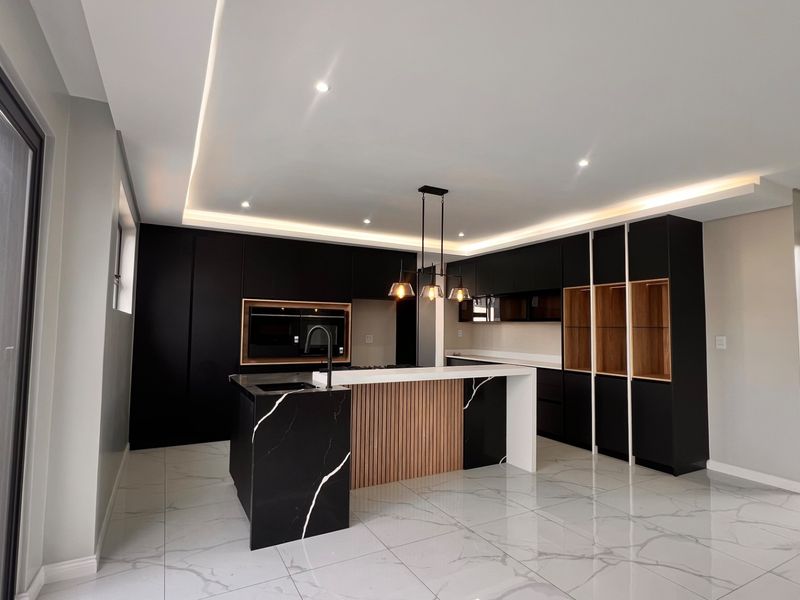 Modern kitchen featuring sleek black cabinetry, a marble-effect island with wood detailing, integrated appliances, and high-end recessed lighting throughout.