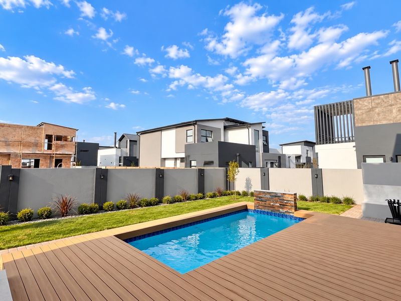 Modern outdoor pool area featuring timber decking, a built-in water feature, and a well-maintained garden enclosed by a perimeter wall.