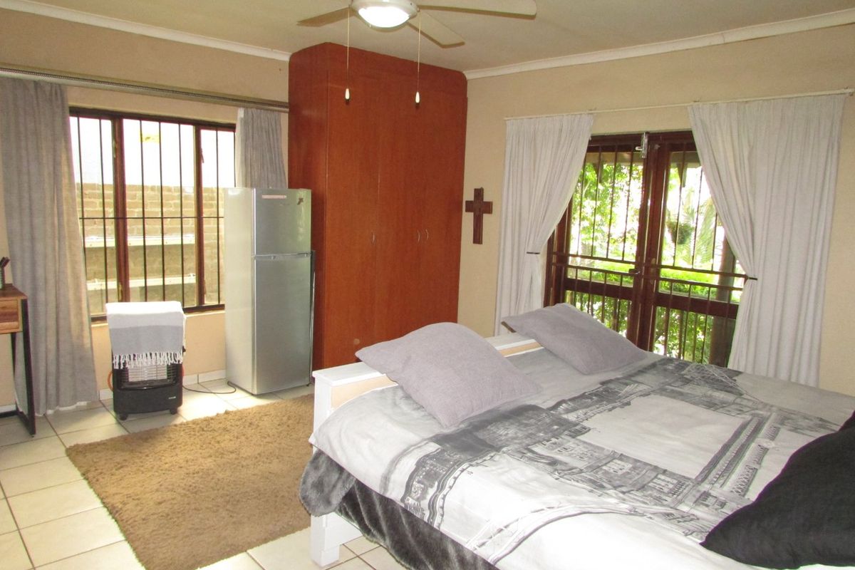 A functional bedroom featuring tiled flooring, a built-in wardrobe, ceiling fan, and direct access to the exterior through a security-fitted door.