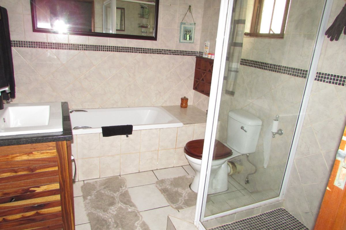 A functional bathroom featuring a tiled bathtub, glass-enclosed shower, built-in vanity, and neutral wall tiling with decorative mosaic accents.