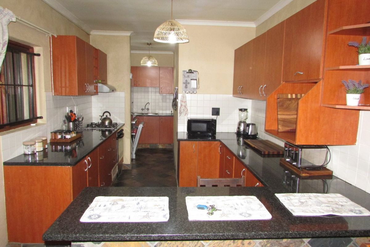 A functional kitchen featuring wooden cabinetry, granite countertops, a tiled backsplash, and a breakfast bar, with an adjoining scullery area.