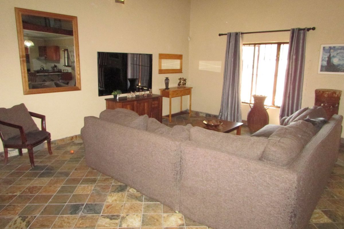 Spacious living room featuring natural stone-style tiled flooring, high ceilings, and an internal window looking through to the kitchen area.