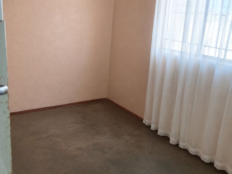 An empty bedroom featuring concrete flooring, peach-toned walls, and a window fitted with security bars.