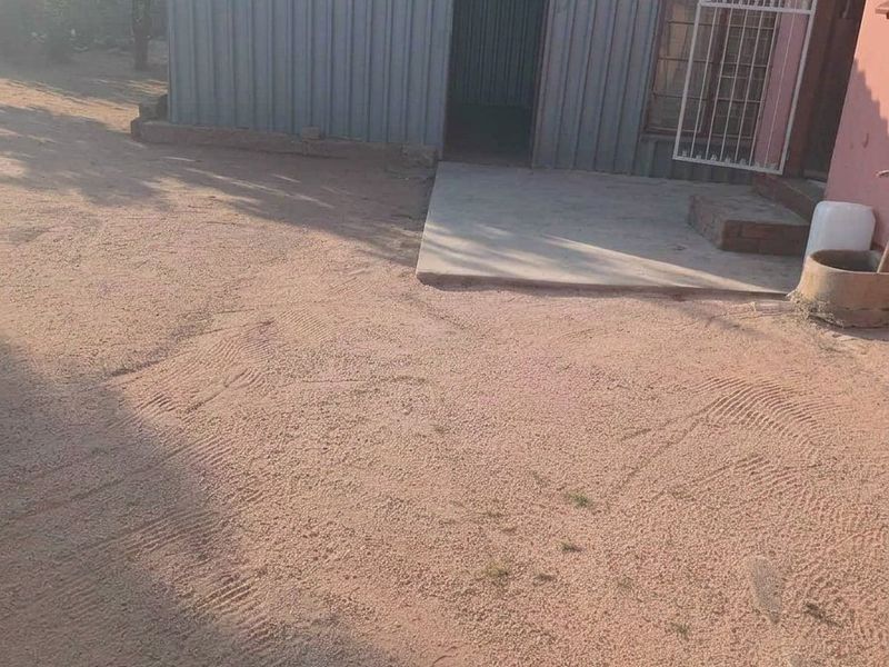 Rear exterior view showing a corrugated metal shed, a concrete patio area, and an unpaved sandy yard.