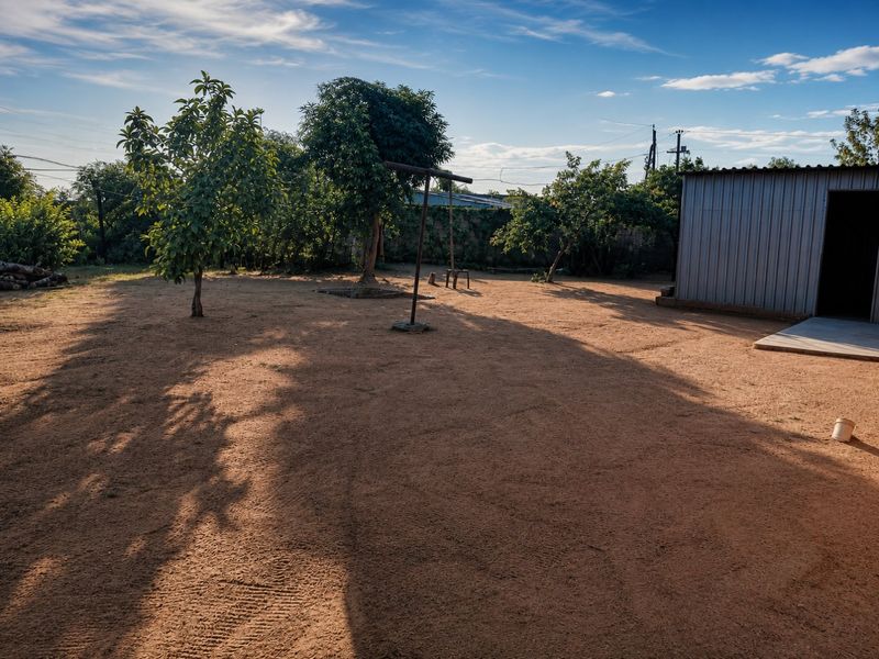 Spacious backyard area featuring a metal storage shed, mature trees, and an open dirt ground surface, offering potential for landscaping and outdoor development.