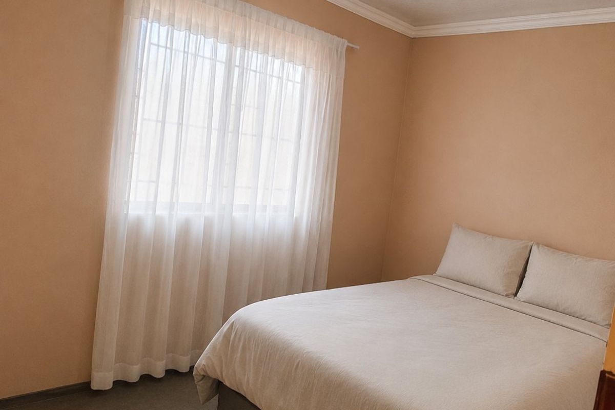 A simple bedroom featuring neutral walls, a window with security bars, and basic ceiling finishes.