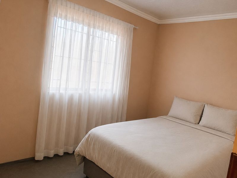 A simple bedroom featuring neutral walls, a window with security bars, and basic ceiling finishes.