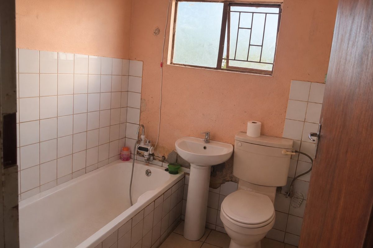 A functional bathroom featuring a bathtub, pedestal basin, and toilet, requiring cosmetic updates to the wall finishes and plaster.