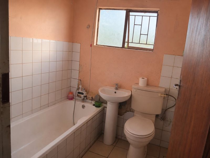 A functional bathroom featuring a bathtub, pedestal basin, and toilet, requiring cosmetic updates to the wall finishes and plaster.