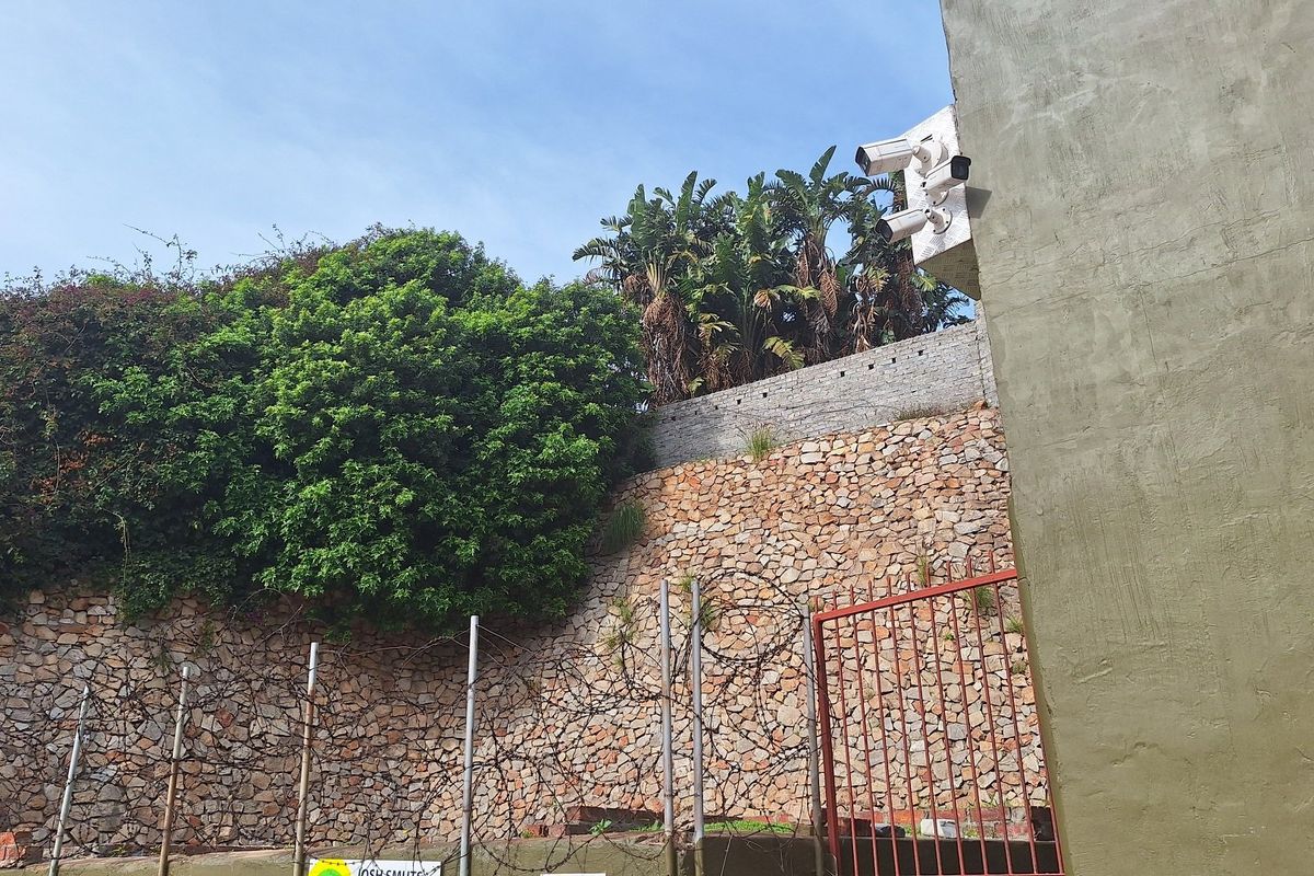Rear exterior view of the commercial property featuring a stone retaining wall, security fencing, and mounted surveillance cameras.