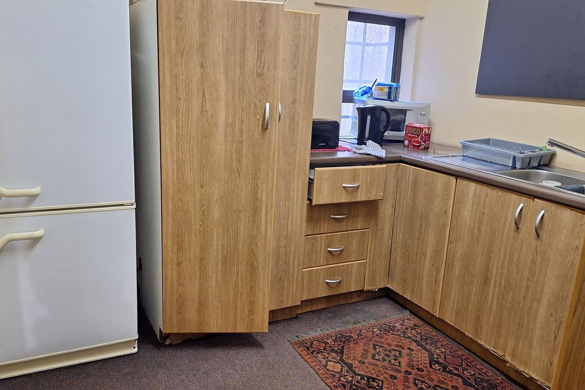 A compact kitchenette featuring wood-look laminate cabinetry, a stainless steel sink, and a laminate countertop, showing signs of wear and tear.