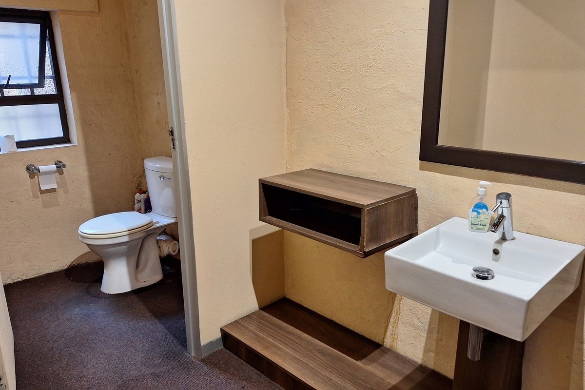 A functional bathroom featuring a pedestal basin, wall-mounted mirror, and separate toilet area with a window for ventilation.