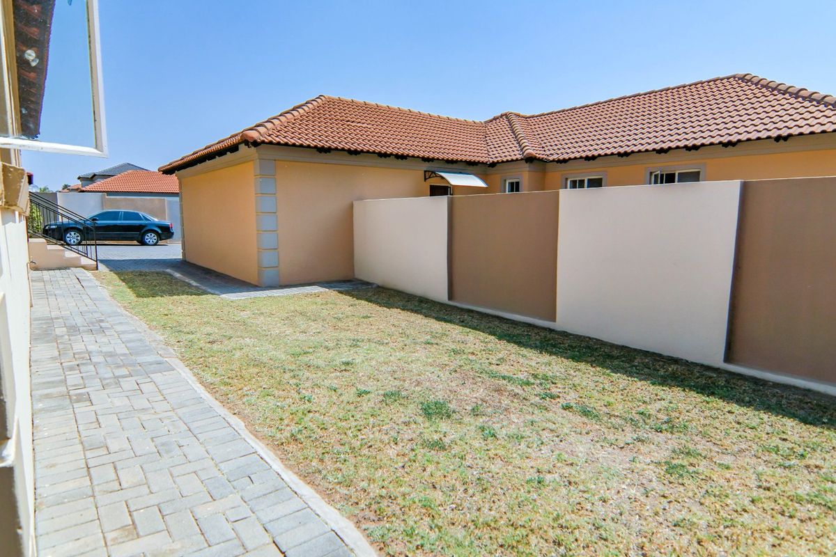 A view of the rear exterior of the townhouse featuring a paved walkway, a small lawn area, and a perimeter boundary wall.