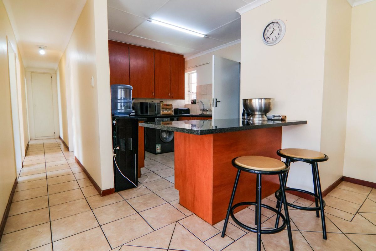 A functional kitchen featuring dark wood cabinetry, granite countertops, a breakfast bar, and tiled flooring, with an adjacent hallway leading to other rooms.