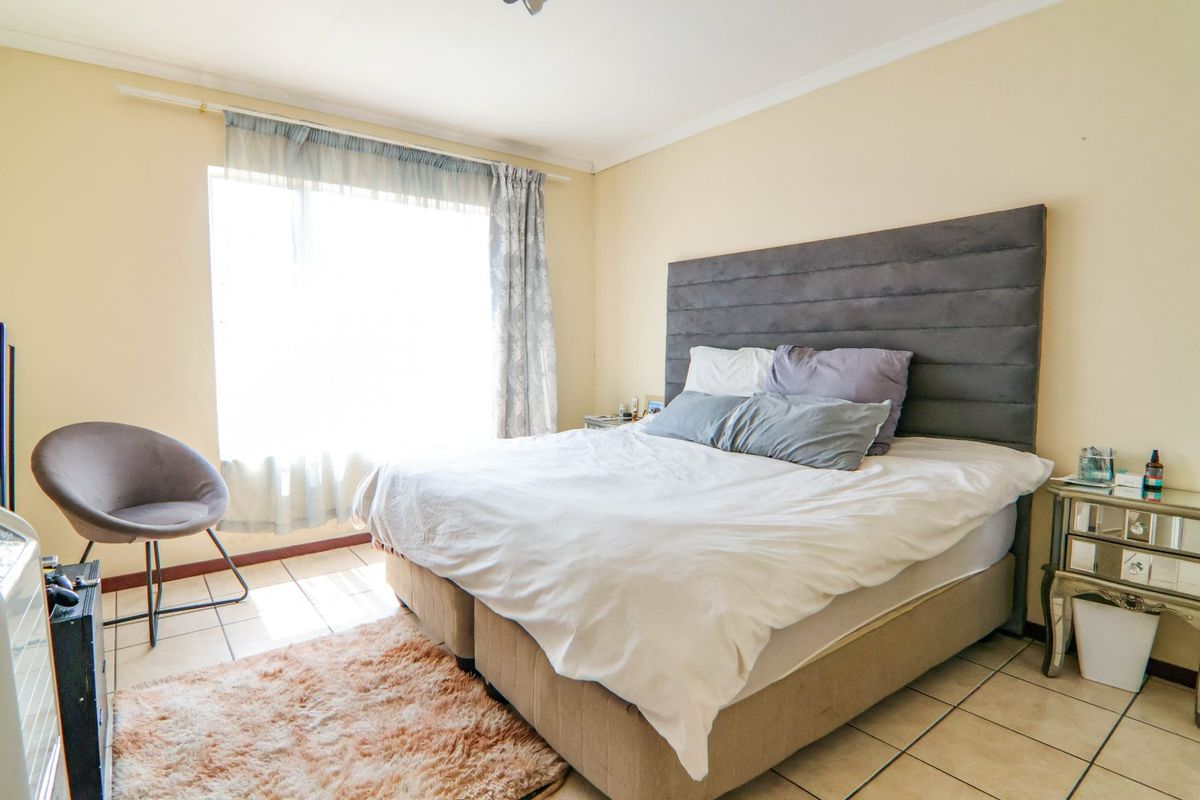 A well-lit bedroom featuring tiled flooring, a large window for natural light, and a neutral color palette.