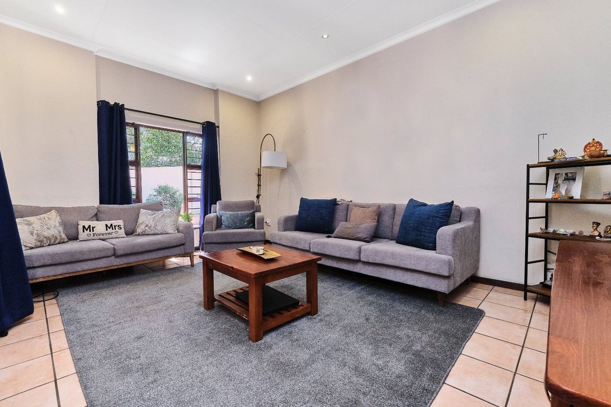 A well-lit living room featuring neutral walls, tiled flooring, and a large window providing natural light.