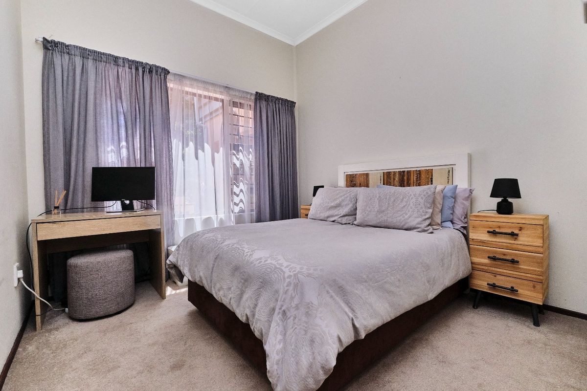 A well-maintained bedroom featuring neutral wall tones, carpeted flooring, and large windows with installed curtain tracks.