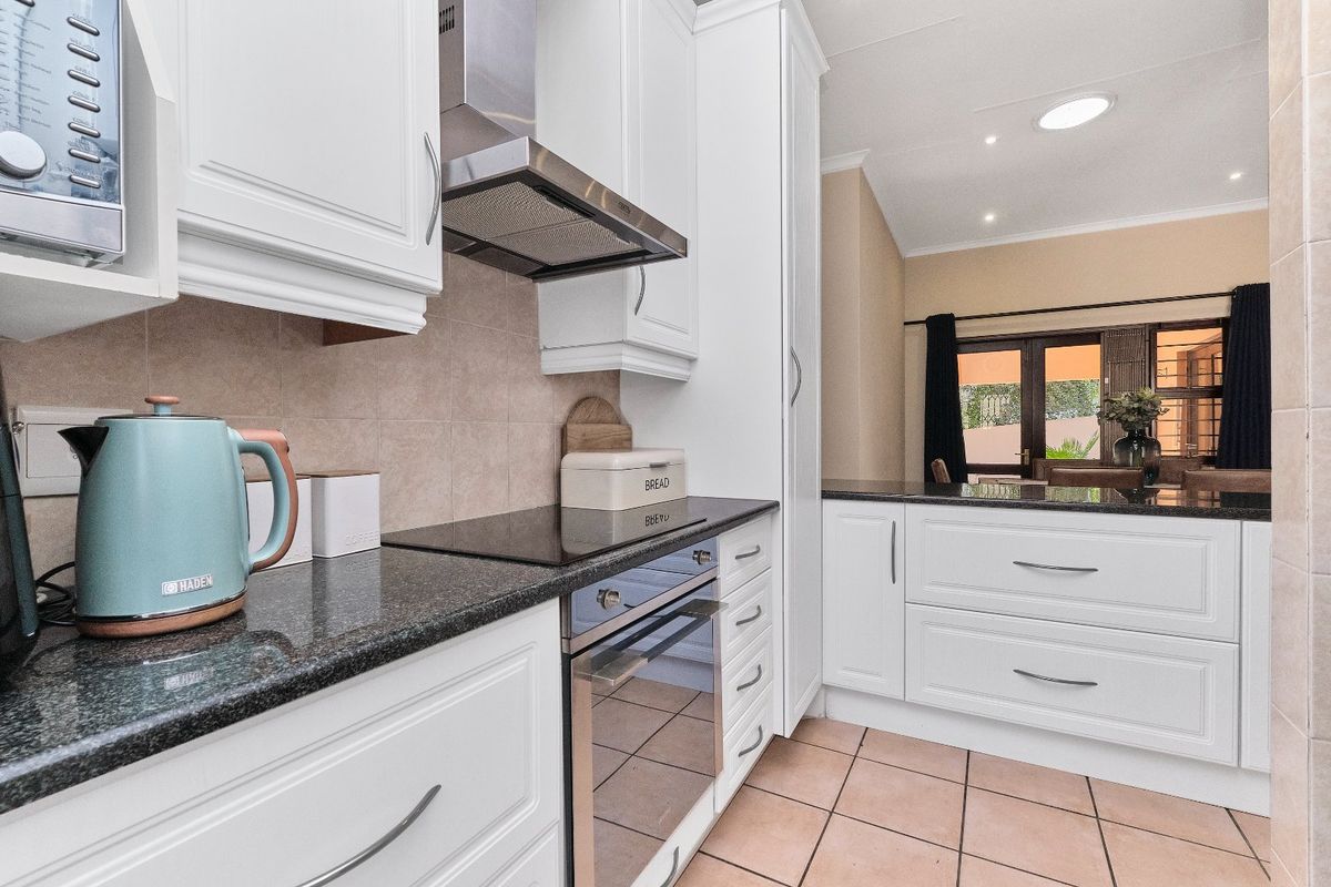 Modern kitchen featuring white cabinetry, granite countertops, built-in oven, electric hob, and tiled flooring, with an open-plan flow to the adjacent living area.