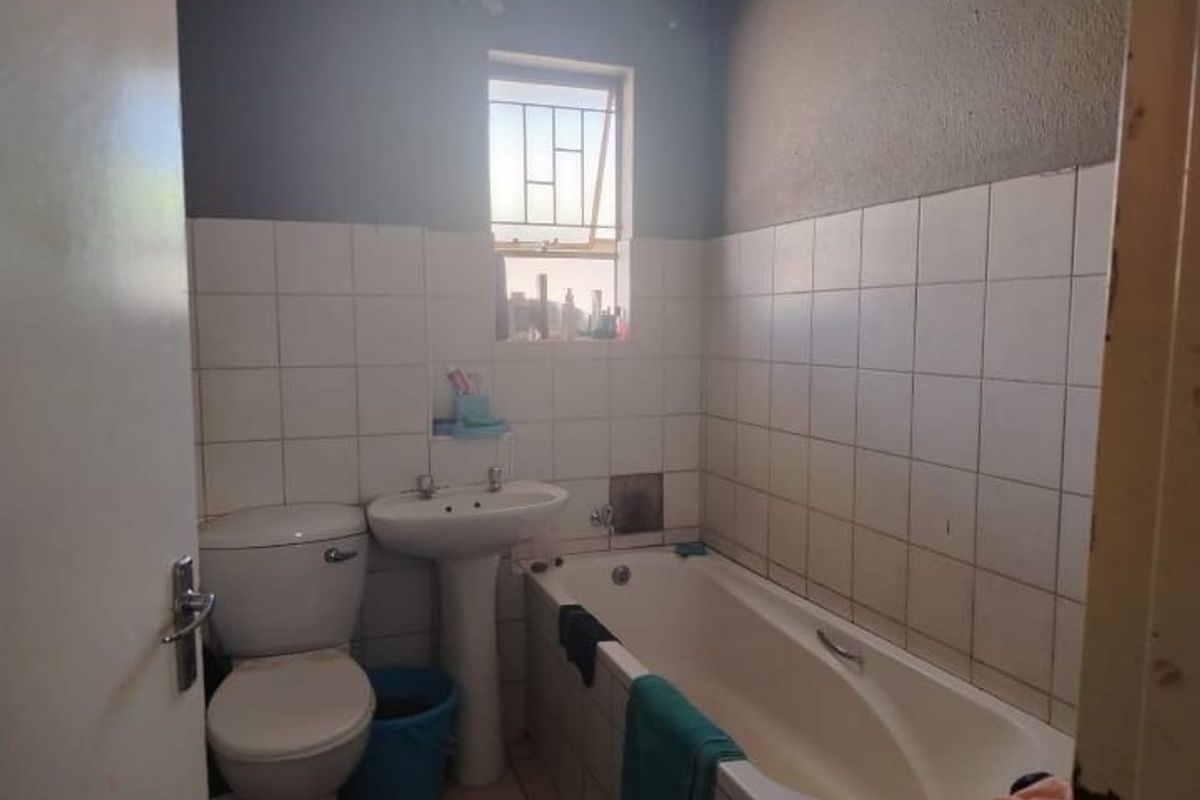 A functional bathroom featuring a pedestal basin, toilet, and bathtub with tiled walls, requiring some cosmetic updates to improve its overall condition.