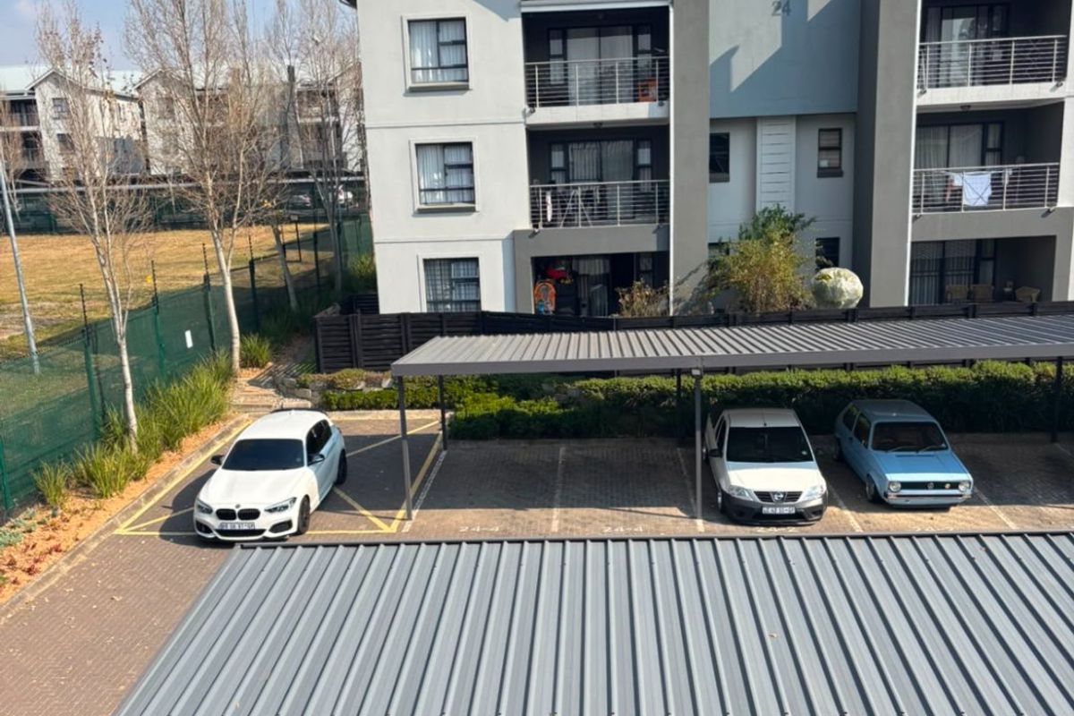 Exterior view of the apartment complex featuring covered parking bays, private balconies, and paved driveway access.