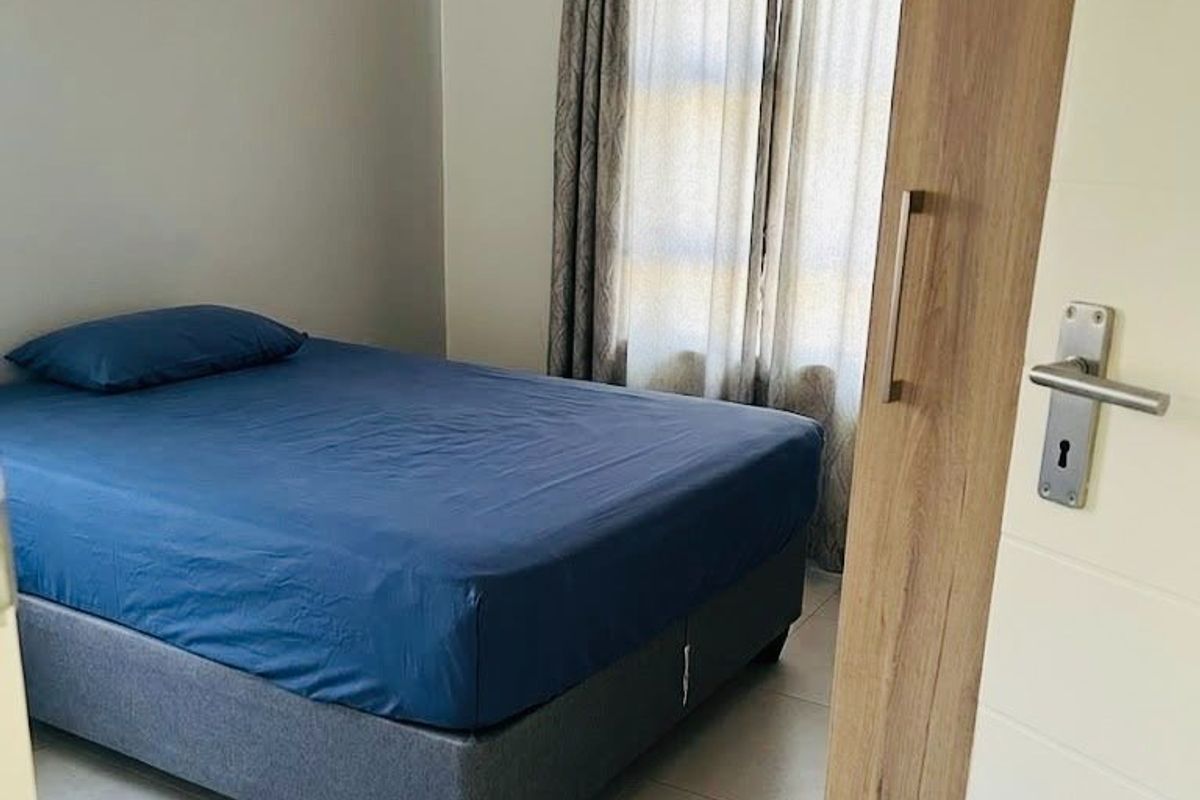 A functional bedroom featuring neutral tiled flooring and natural light through window curtains.