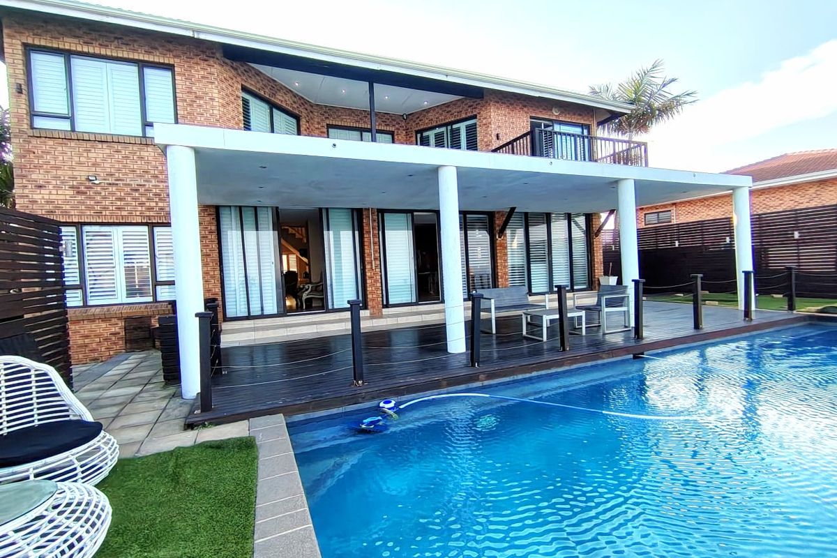 Rear view of a two-story brick house featuring a swimming pool, expansive timber decking, and a covered patio area with sliding door access.