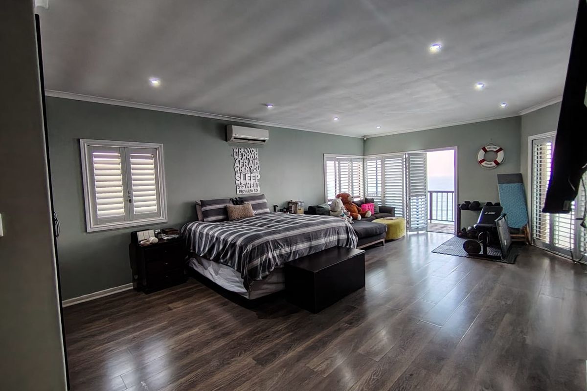 Spacious bedroom featuring dark laminate flooring, recessed lighting, split-system air conditioning, and plantation shutters with direct access to a balcony.