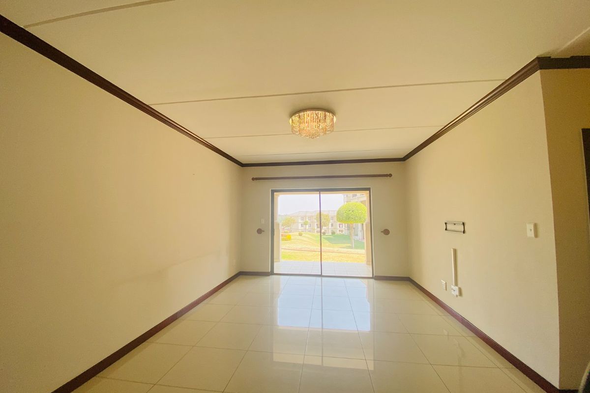 A bright, empty living room featuring tiled floors, crown molding, and a sliding glass door leading to an outdoor area.