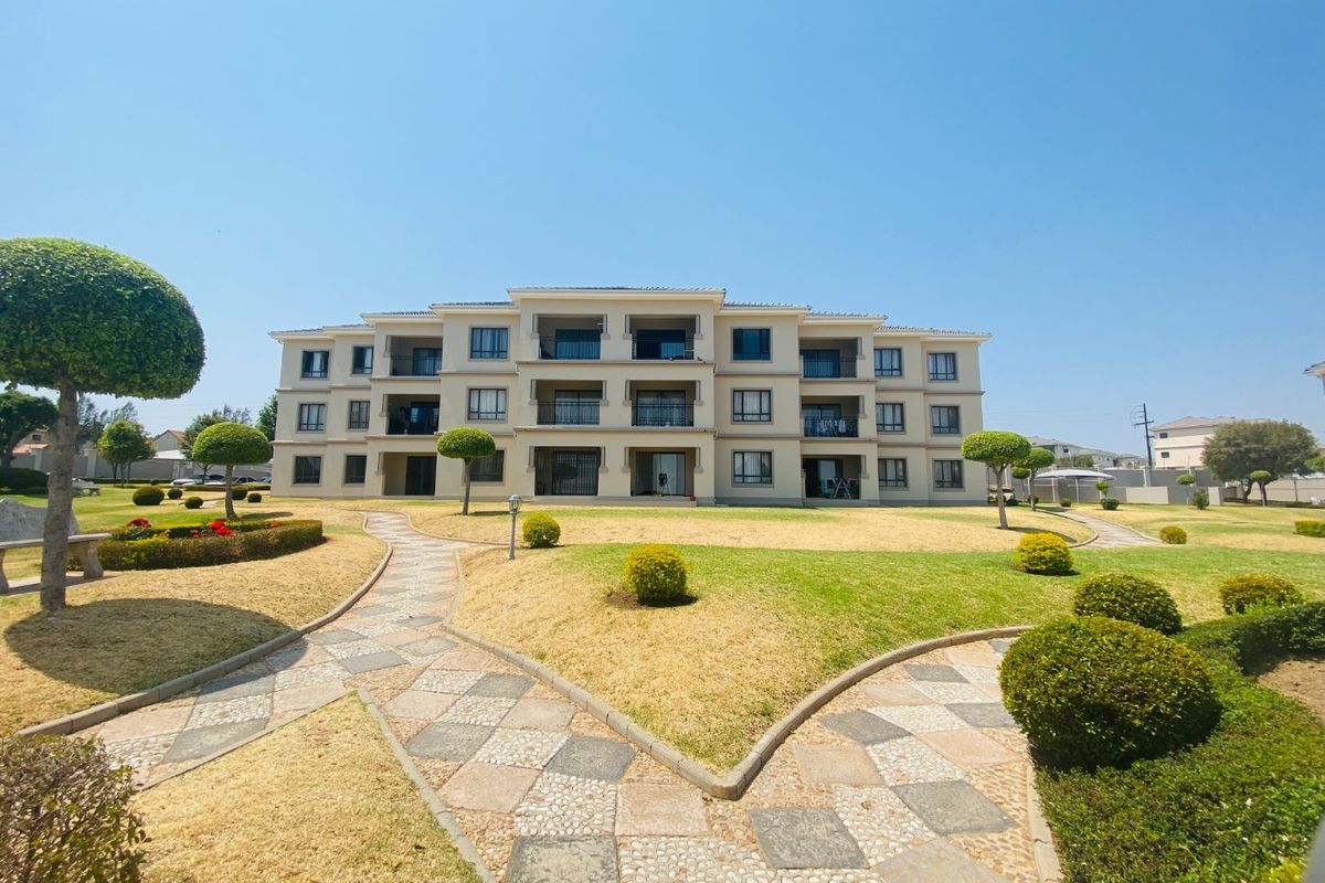 A well-maintained multi-story apartment building featuring private balconies, surrounded by landscaped gardens and paved walkways.
