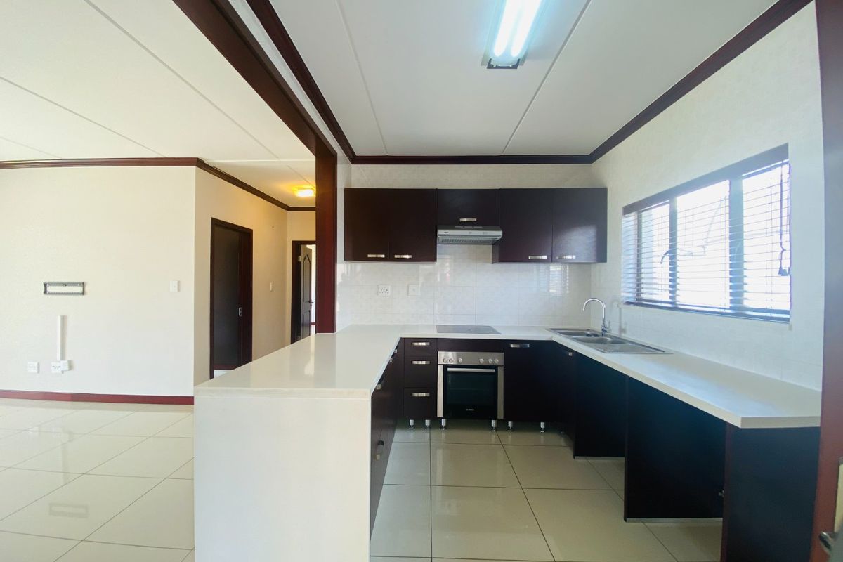 A clean, modern kitchen featuring dark cabinetry, white quartz countertops, built-in oven and hob, and tiled flooring in an open-plan layout.