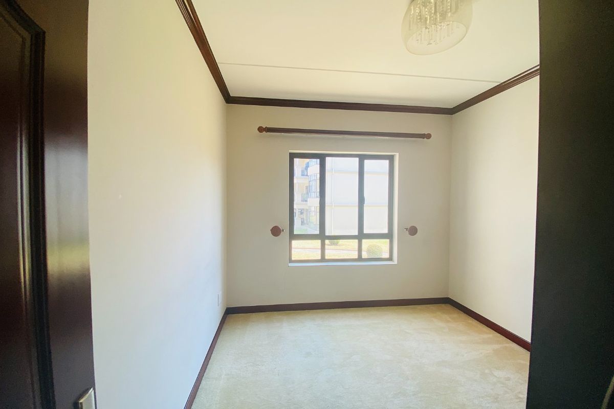 A clean, empty bedroom featuring neutral carpeting, crown molding, and a window with a curtain rod, offering a blank canvas for personalization.