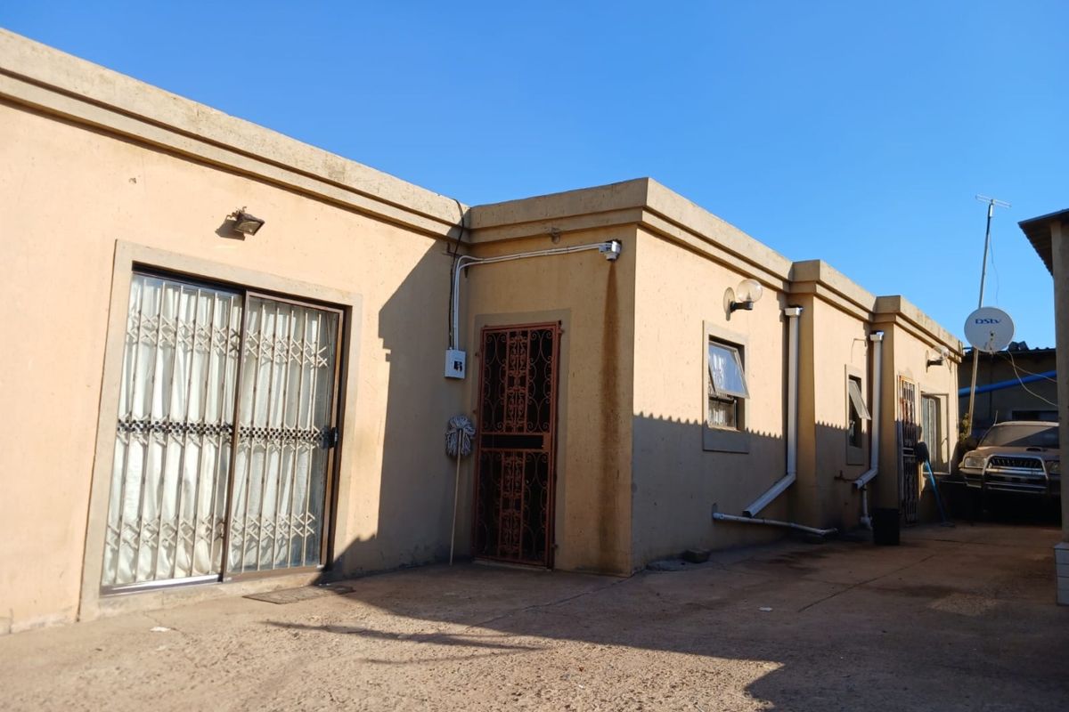 Rear exterior view of the property featuring concrete paving, sliding glass doors with security gates, and external wall lighting.