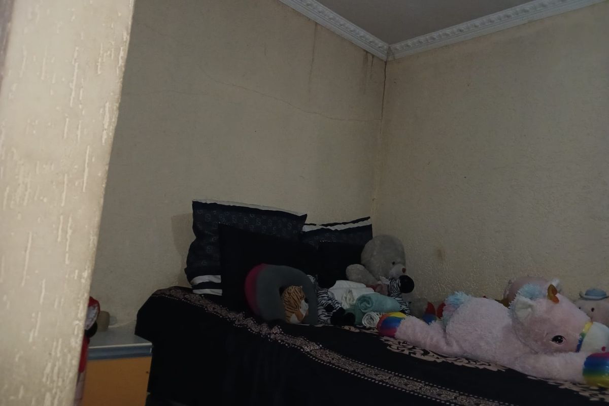 A bedroom featuring decorative ceiling cornicing, currently showing signs of wall cracking and water staining that require maintenance and repair.