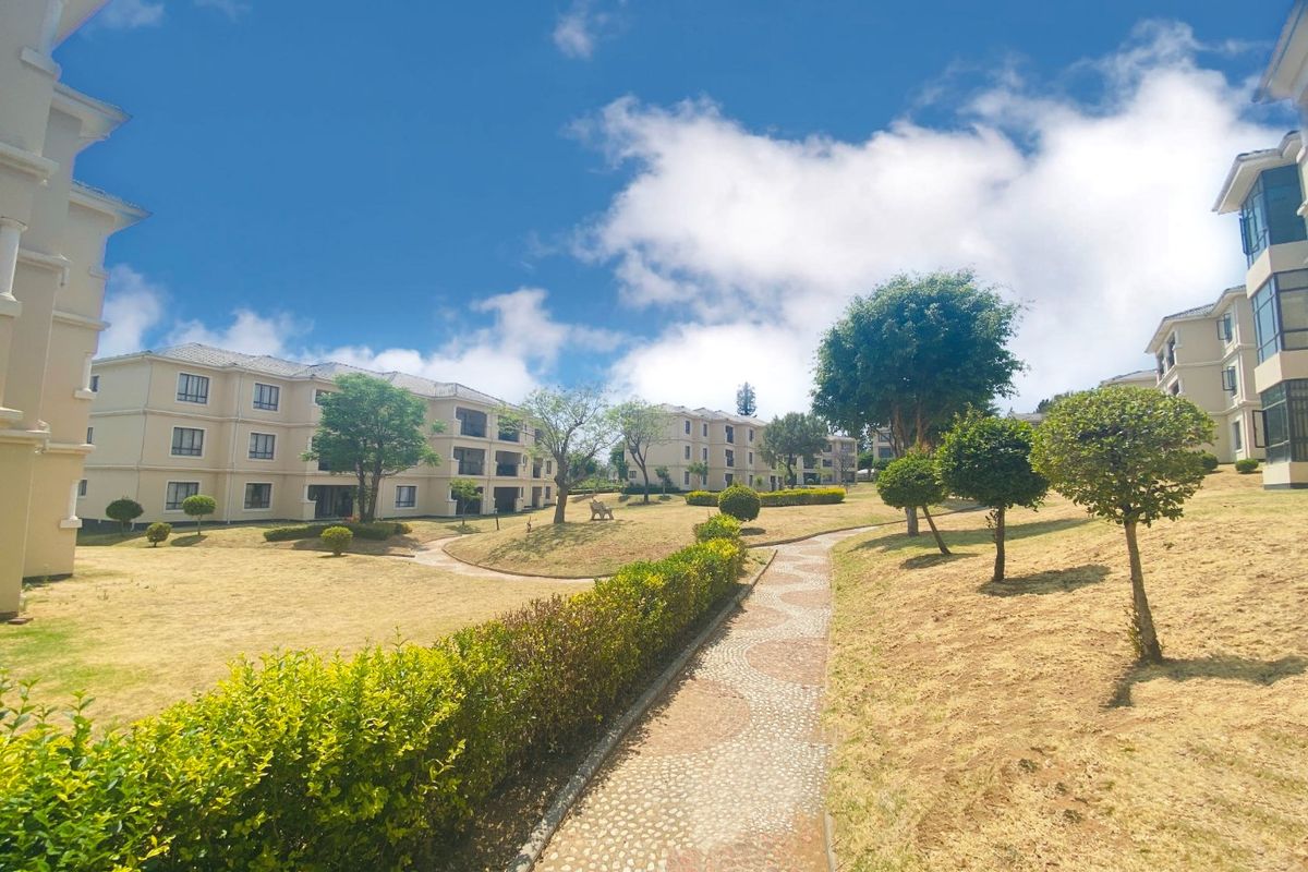 A view of the apartment complex grounds featuring landscaped gardens, manicured hedges, and a paved walkway connecting the residential buildings.