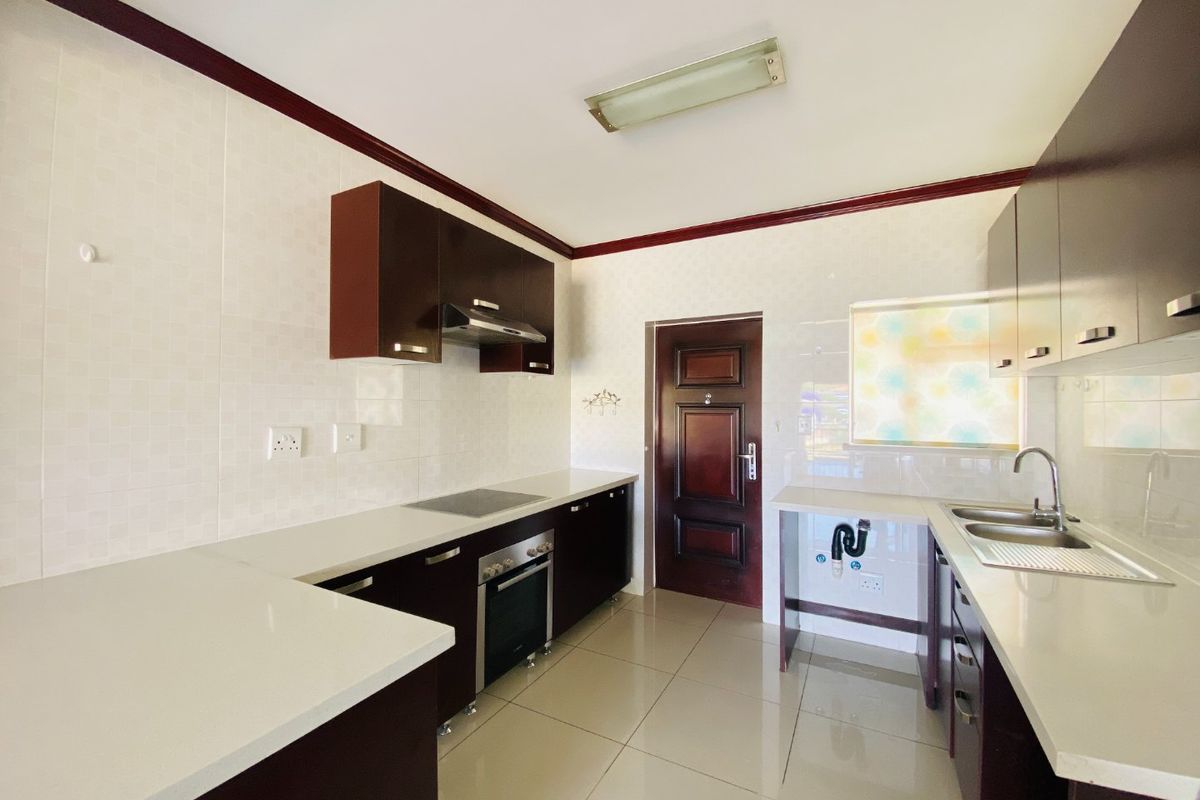 A clean, modern kitchen featuring dark cabinetry, white stone countertops, integrated oven and hob, and tiled finishes throughout.
