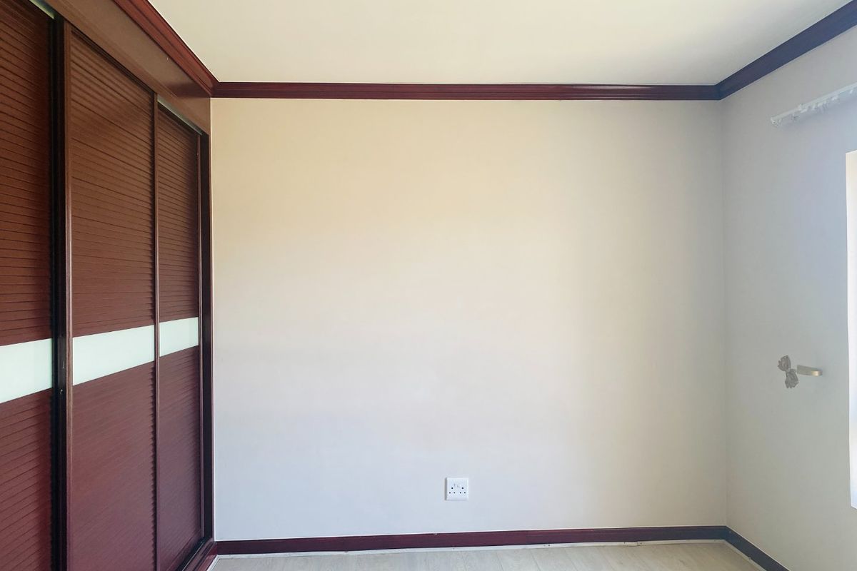 A clean, empty bedroom featuring built-in sliding door wardrobes, timber-look laminate flooring, and dark timber trim detailing.