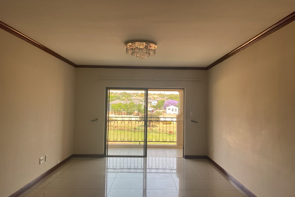 An empty, well-lit living room featuring polished tile floors, crown molding, and a sliding glass door leading to a balcony with neighborhood views.