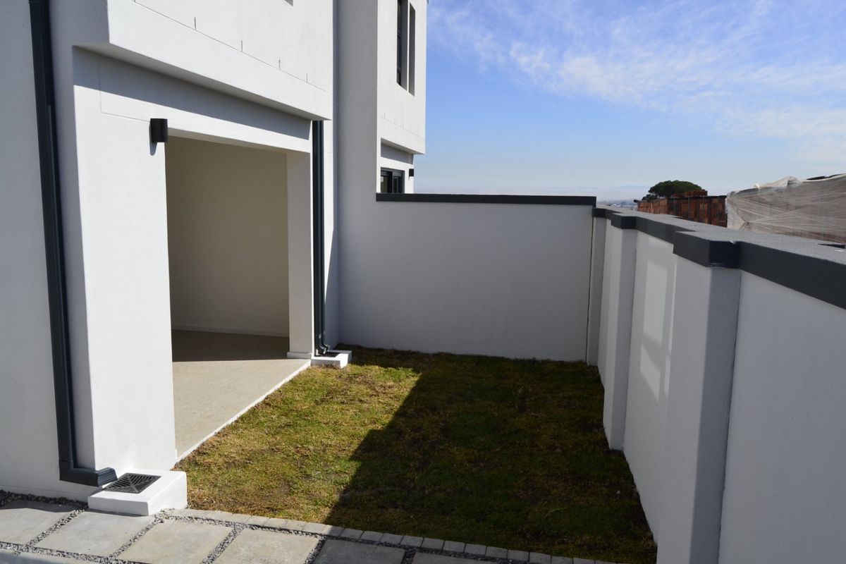 A private rear courtyard featuring a small lawn area, paved patio section, and modern boundary walls.