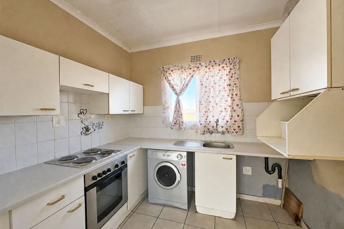 A functional kitchen featuring white cabinetry, an electric hob, built-in oven, and stainless steel sink, requiring some cosmetic updates to the cabinetry and wall finishes.